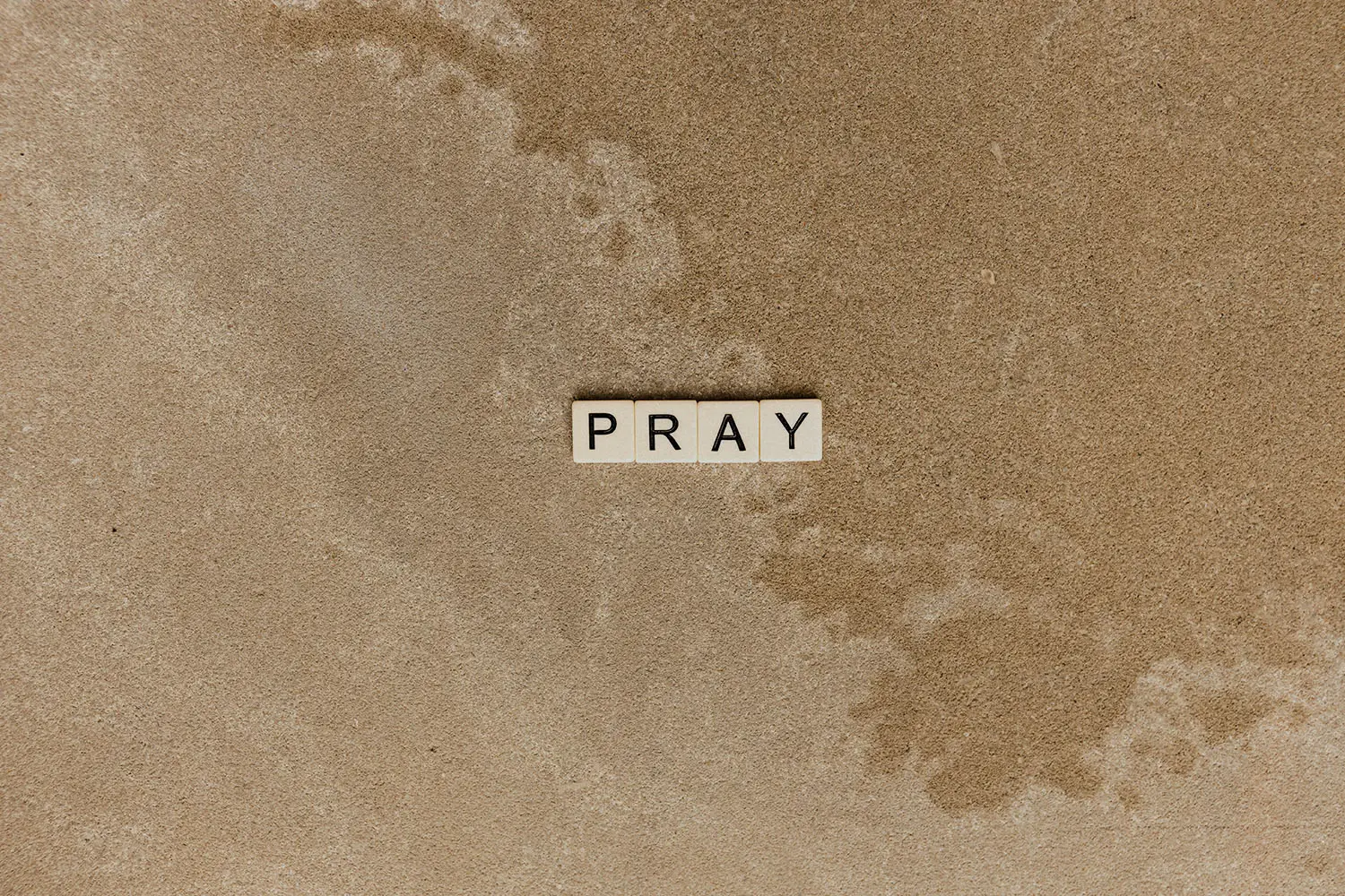 Scrabble letters spelling "PRAY" with an outline of a map in the background