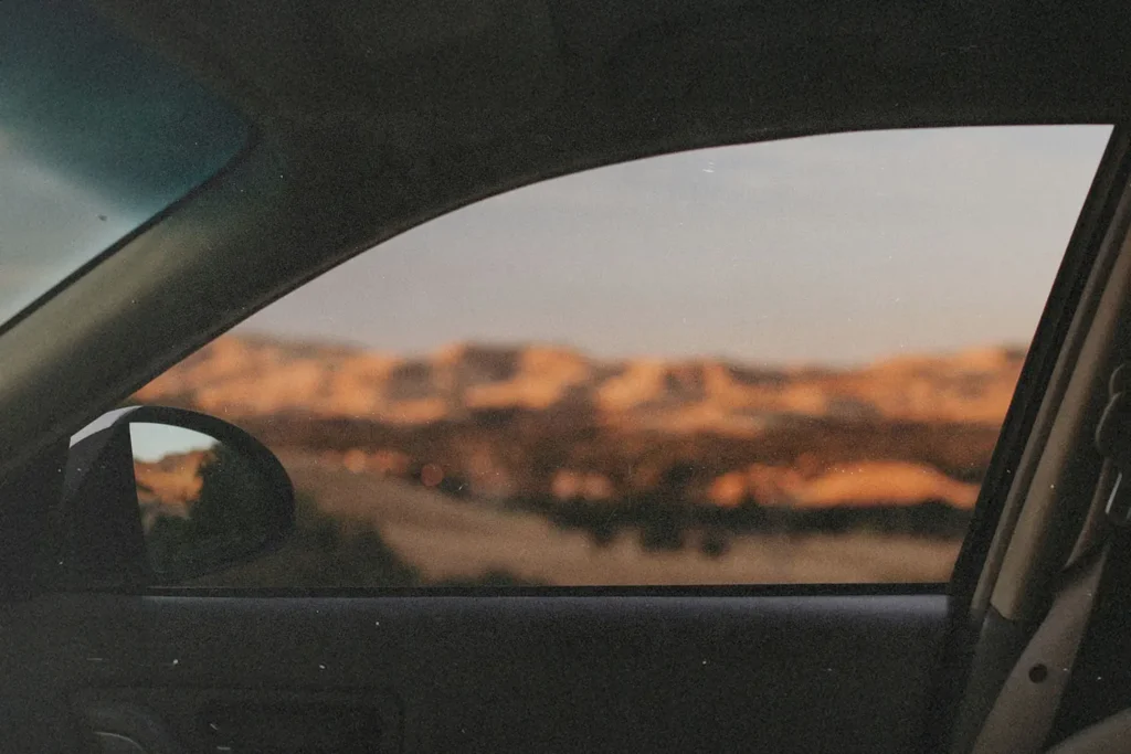 A view from inside a car looking out through the side window at a distant landscape, with sunlit hills and open countryside appearing softly out of focus