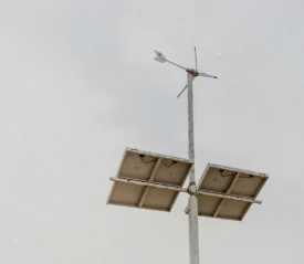Solar panels mounted on a tall pole with a small wind turbine against a pale sky.