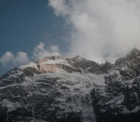 Snow on a rocky mountain with a cloudy blue sky in the background