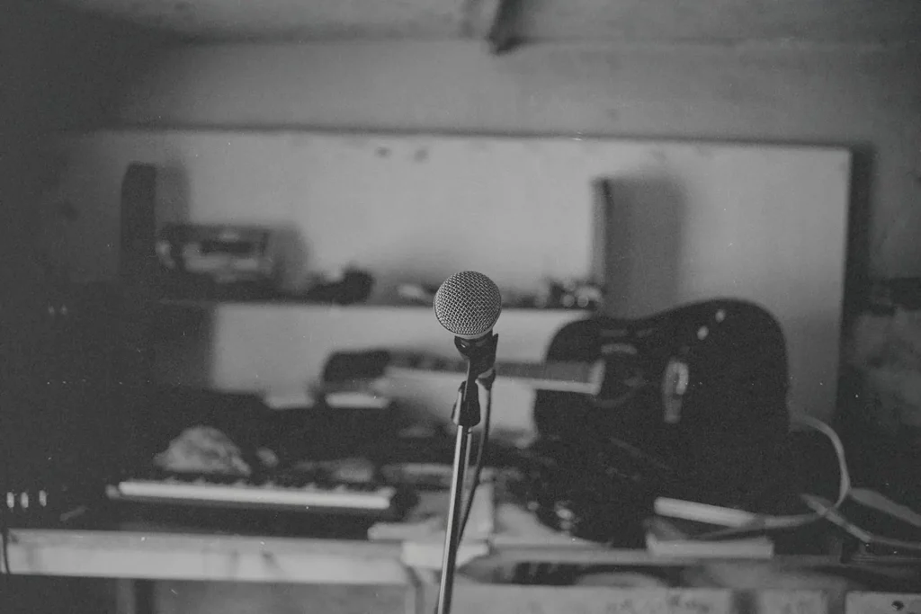 Single microphone on a stand in the center of a dimly lit room filled with musical instruments and equipment