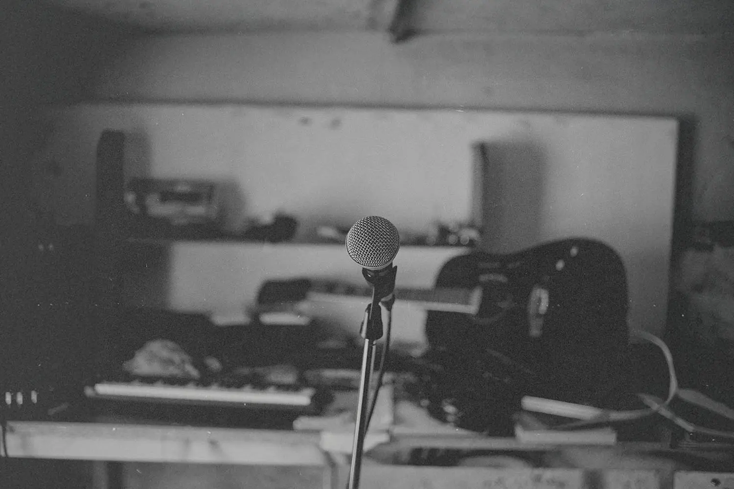 Single microphone on a stand in the center of a dimly lit room filled with musical instruments and equipment