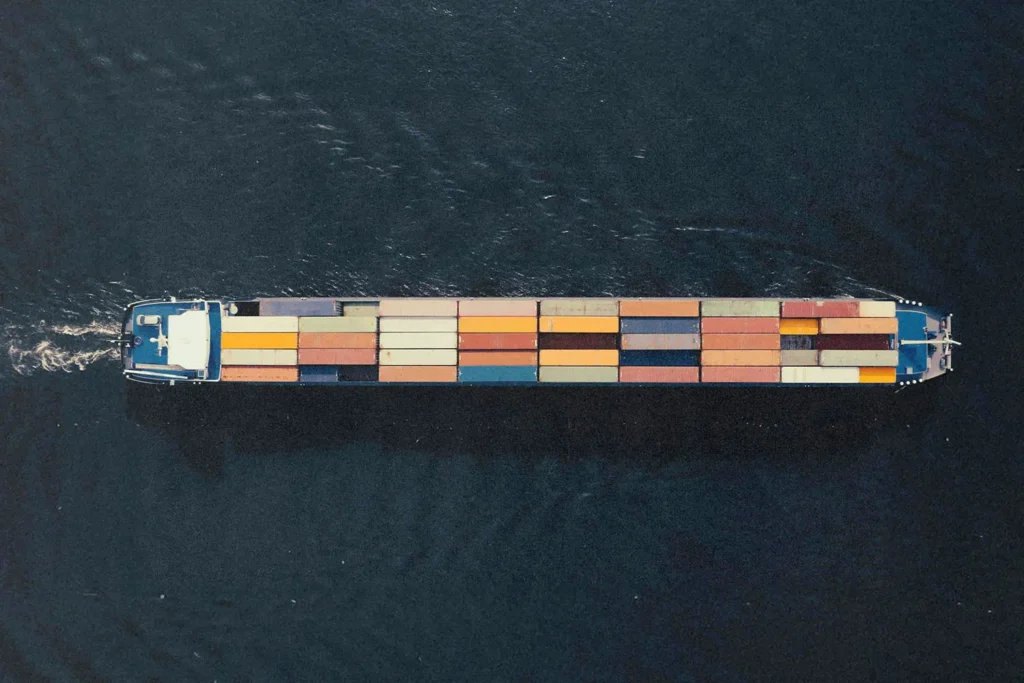 Aerial view of a long cargo ship carrying colorful shipping containers across dark water