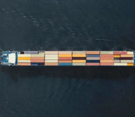 Aerial view of a long cargo ship carrying colorful shipping containers across dark water