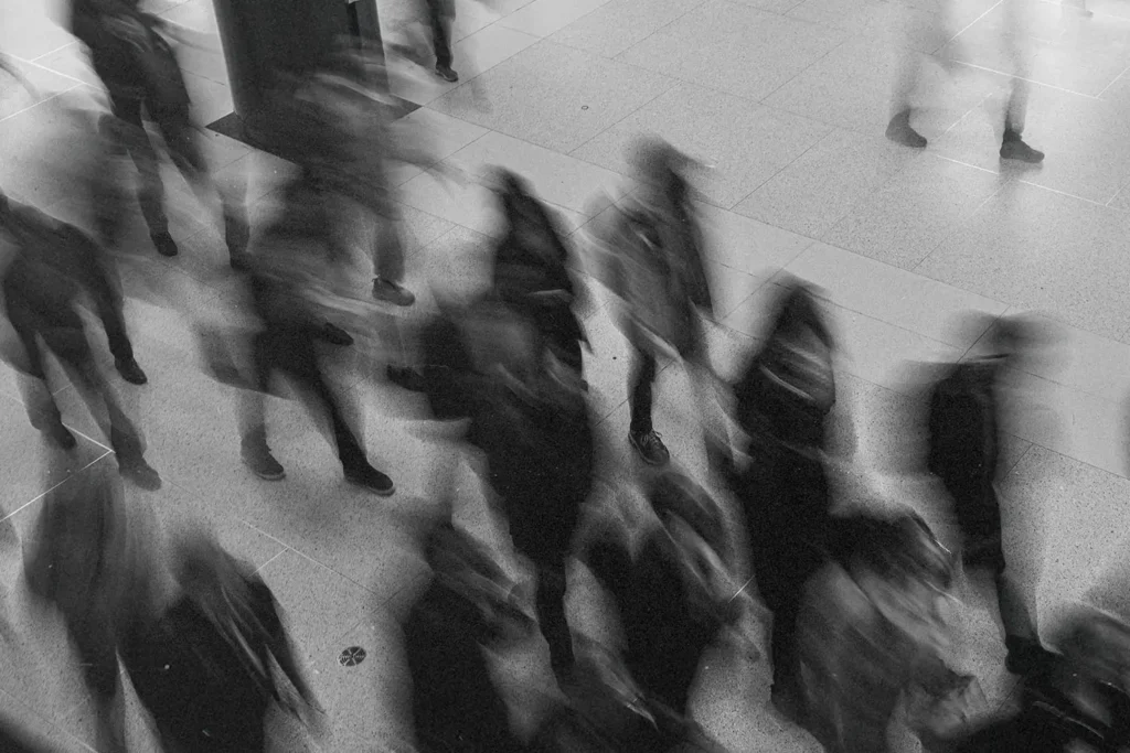 Black‑and‑white motion‑blurred photo of people walking through a public indoor space
