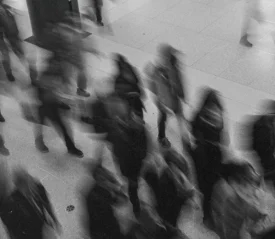 Black‑and‑white motion‑blurred photo of people walking through a public indoor space