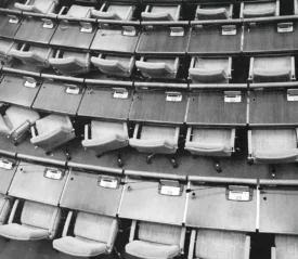 Rows of empty auditorium seats with attached wooden desks arranged in curved tiers