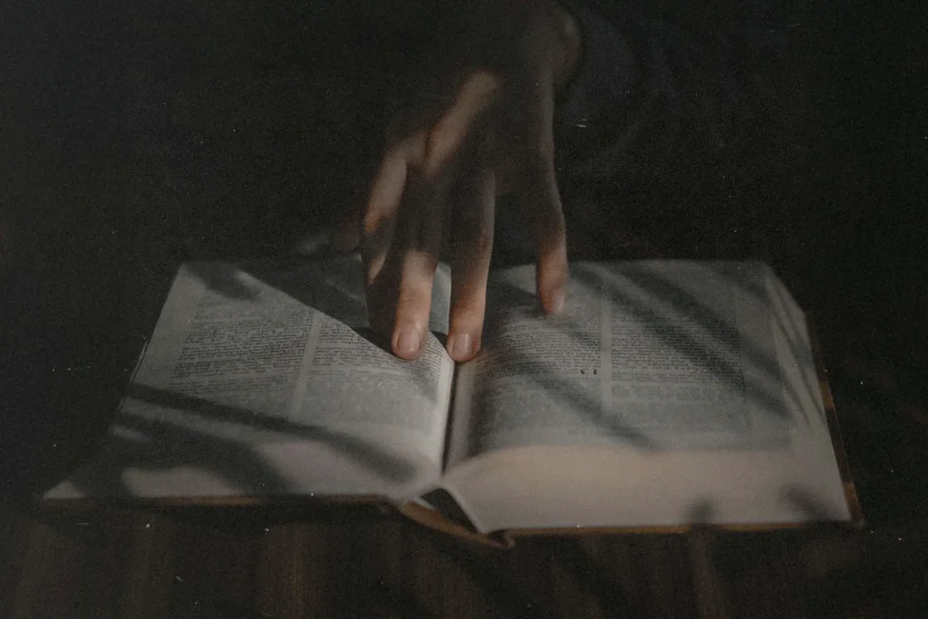 Hand resting on the open pages of a book in low, moody light.