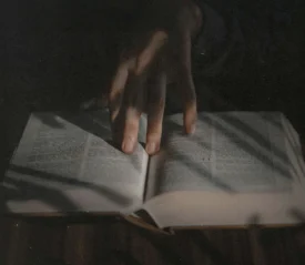 Hand resting on the open pages of a book in low, moody light.
