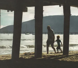 dad and son walking the beach under a pier