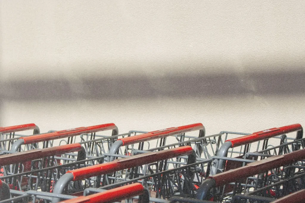A row of shopping carts with red handles sits in soft sunlight beside a blank wall