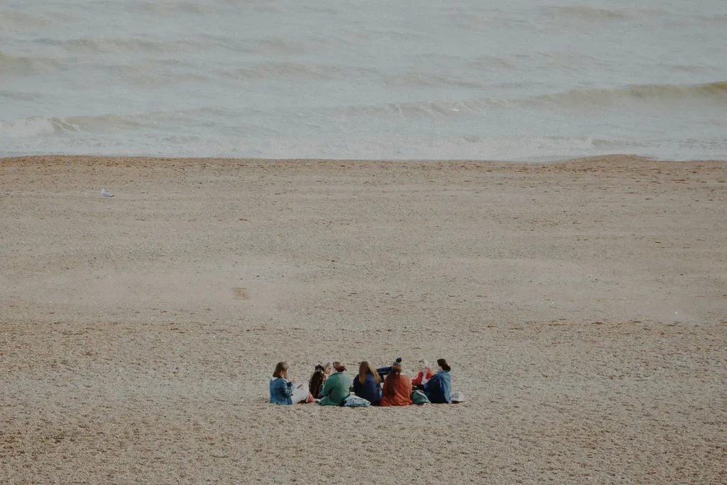 Group of people sitting in a circle in the sand with the ocean in the distance