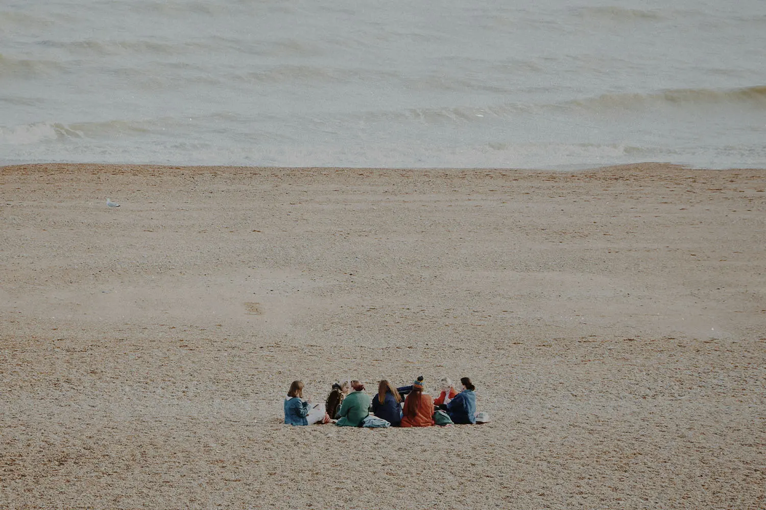 Group of people sitting in a circle in the sand with the ocean in the distance