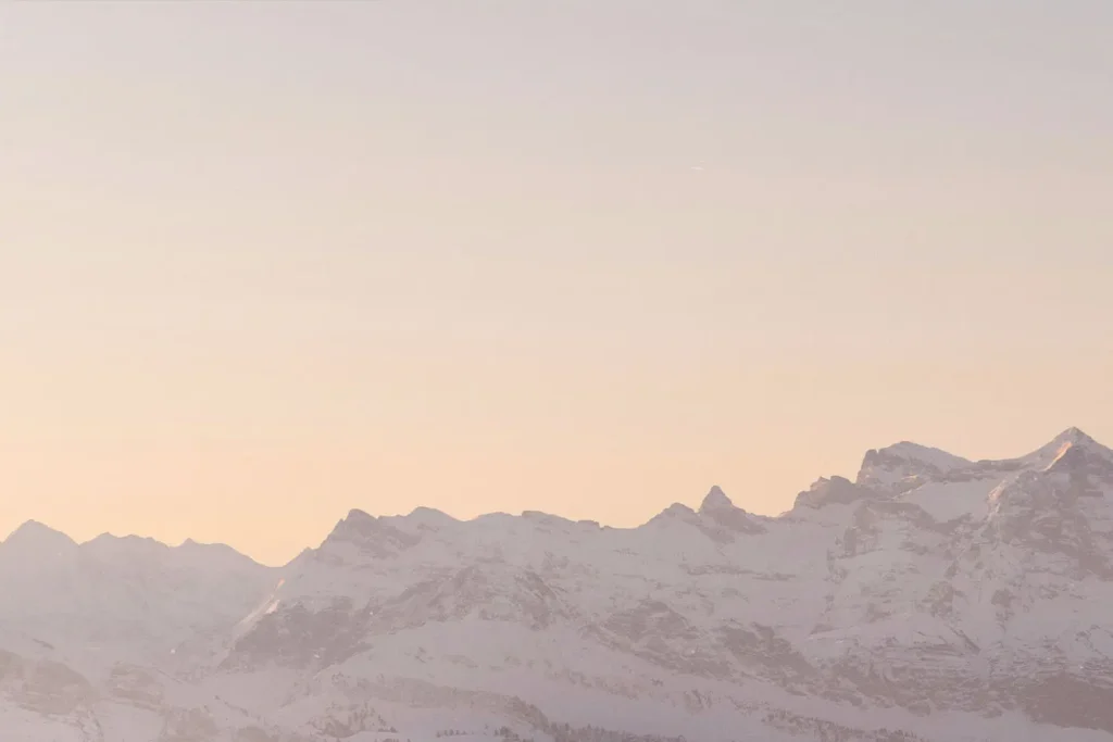 Snow-covered mountain range under a soft pastel sunrise sky