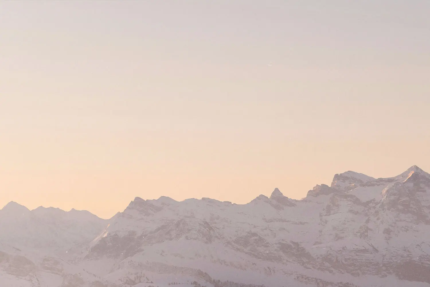Snow-covered mountain range under a soft pastel sunrise sky