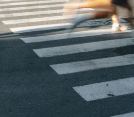A blurred figure runs across a crosswalk, leaving a streak of motion over the white painted stripes on the pavement