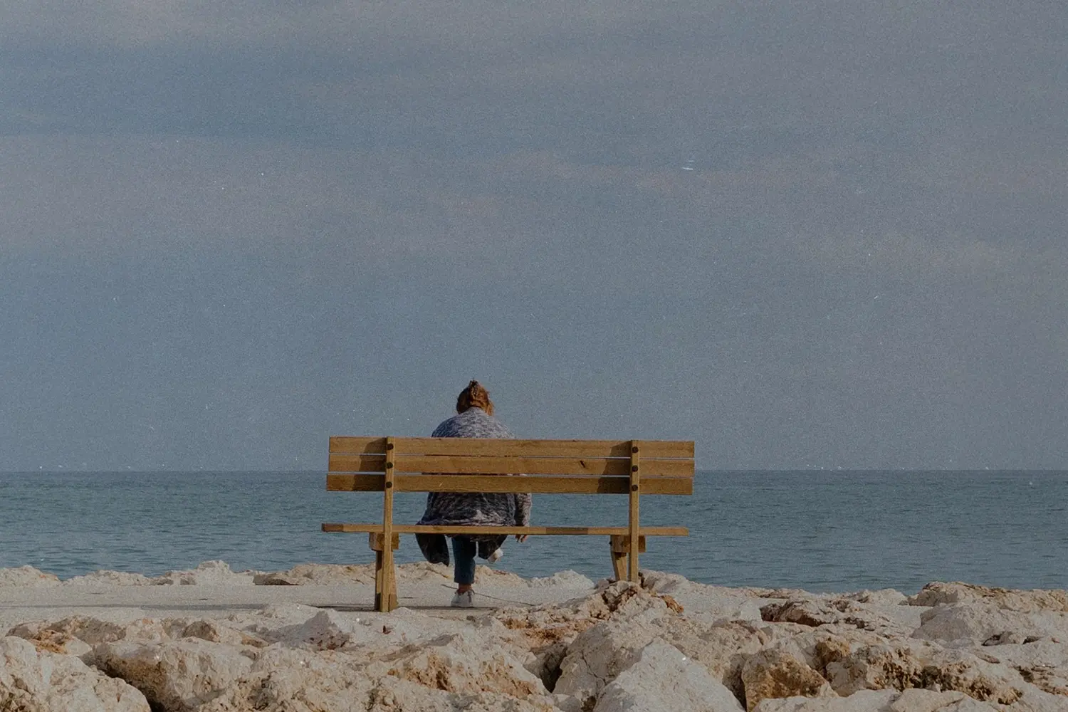 woman sitting alone on a bench on a rocky beach