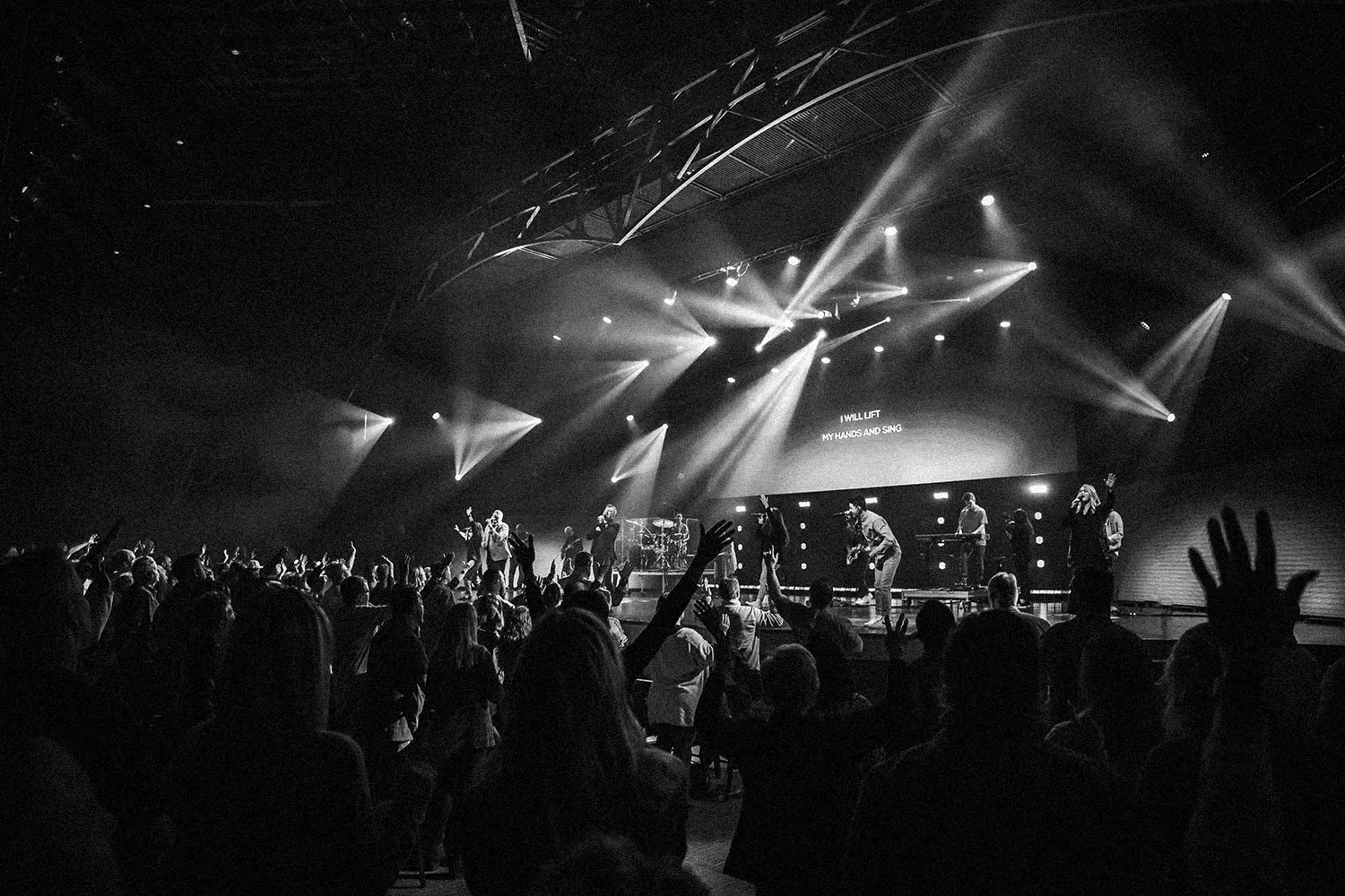 Crowd of people worshiping as band sings on stage
