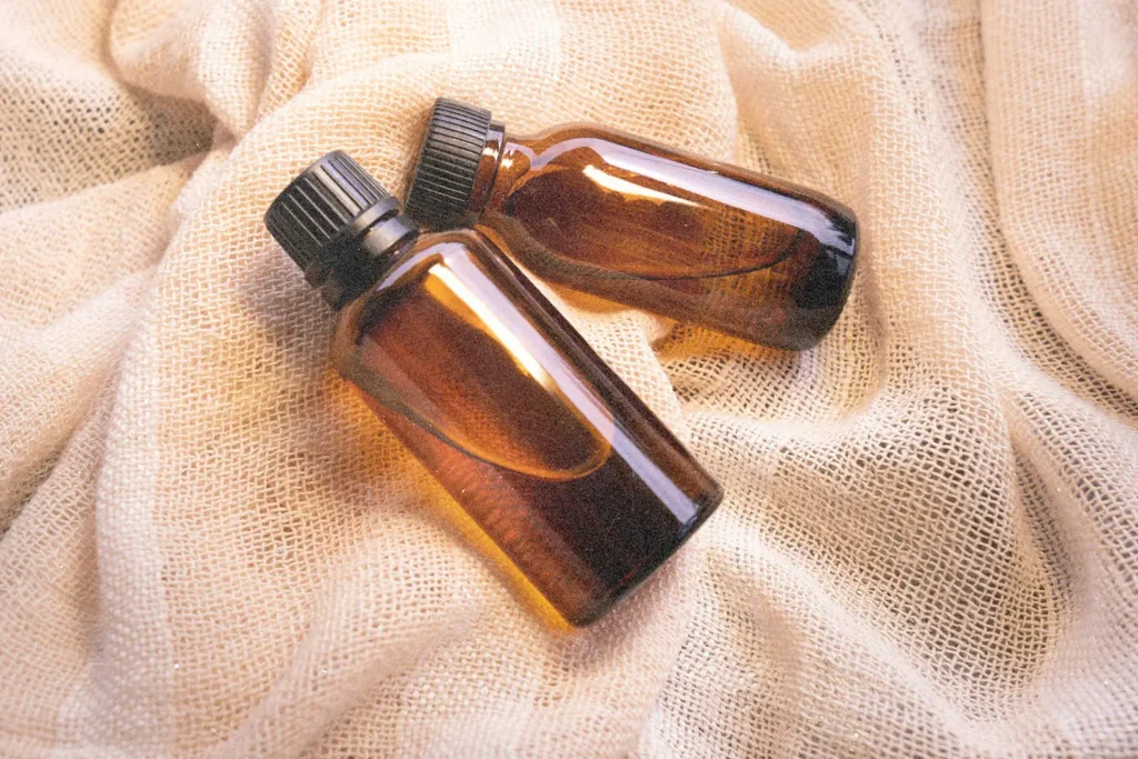 Two amber glass bottles with black caps lie on a textured cream-colored fabric