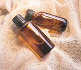 Two amber glass bottles with black caps lie on a textured cream-colored fabric