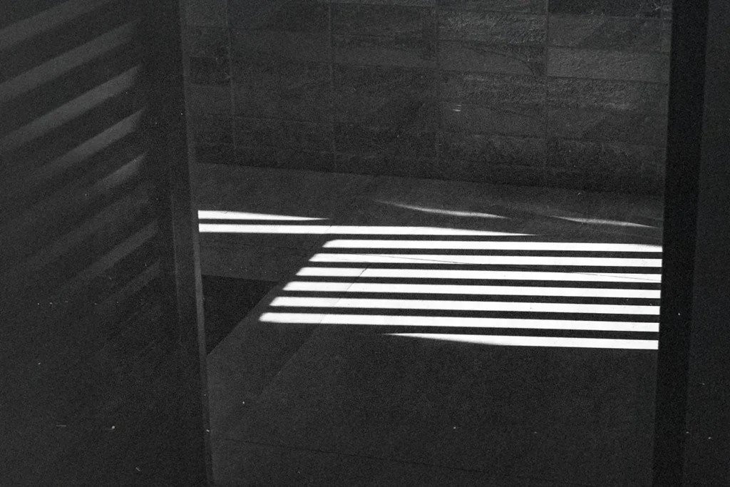 Bright horizontal light beams creating striped shadows across a tiled floor and wall