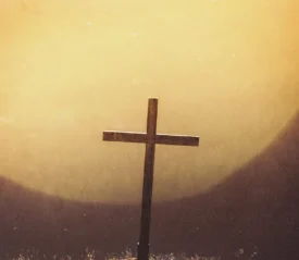 Wooden cross standing in front of a glowing golden light, creating a warm and reverent atmosphere