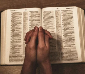 praying hands on top of an open bible