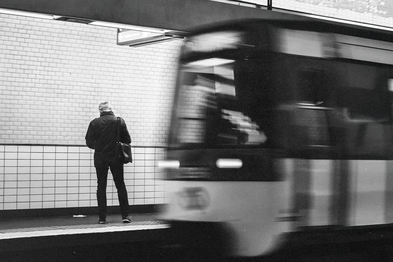 Person standing on a subway platform as a train speeds past in motion blur