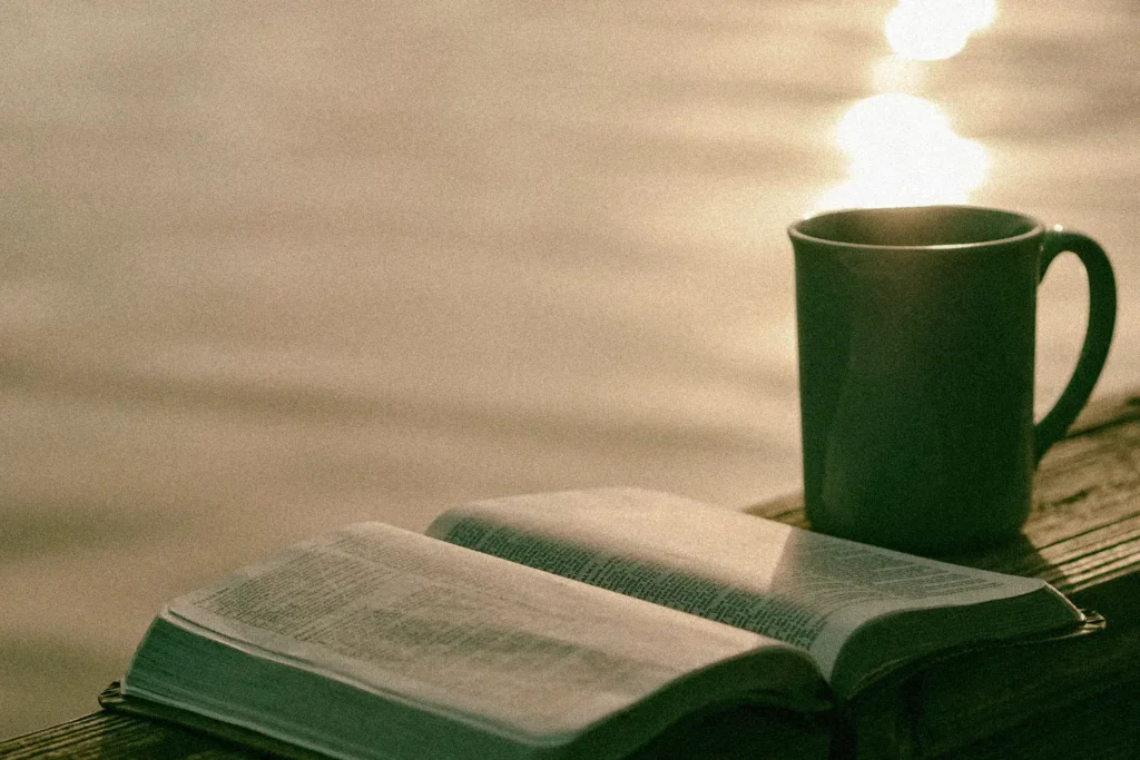 Coffee mug and open Bible on wooden ledge overlooking a body of water