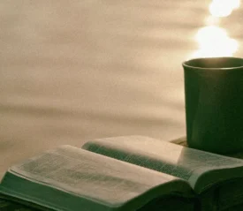 Coffee mug and open Bible on wooden ledge overlooking a body of water