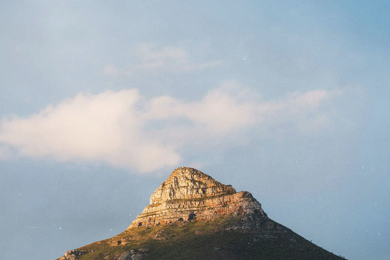 Sunlit rocky mountain peak rising against a soft blue sky with scattered clouds
