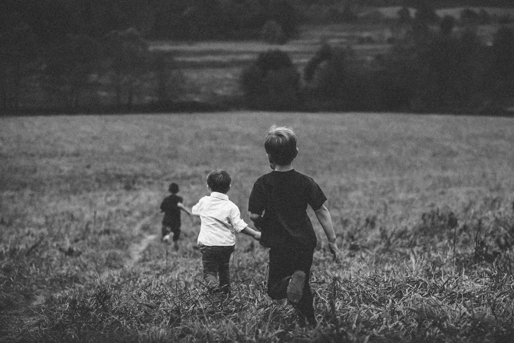 Three boys holding hands running through a field