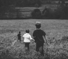 Three boys holding hands running through a field