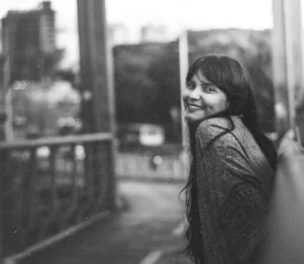 Person standing on a bridge overlooking a city street in a soft, black‑and‑white scene