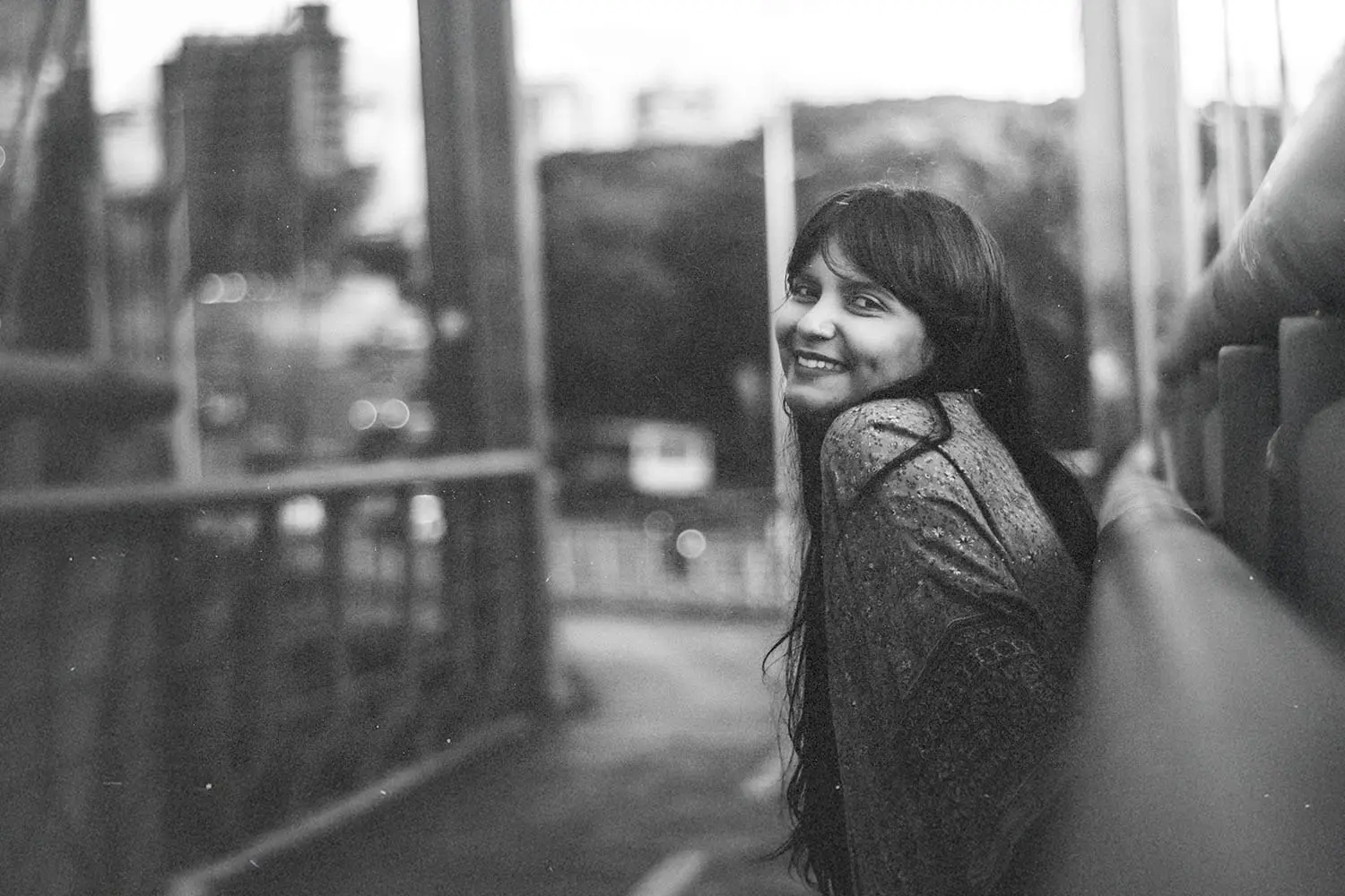 Person standing on a bridge overlooking a city street in a soft, black‑and‑white scene