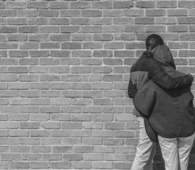 two people hugging while looking at a brick wall