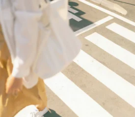 Person in a yellow dress and white jacket walking on a crosswalk