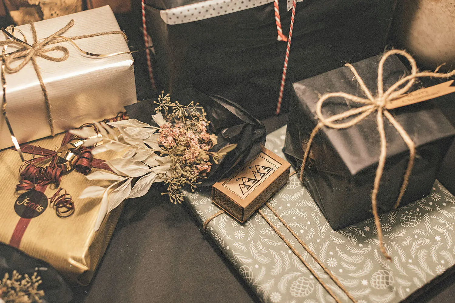 Collection of beautifully wrapped gifts in various decorative papers and twine, accented with dried flowers and festive tags