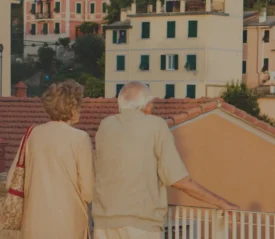 Back of an elderly couple standing on a balcony overlooking city buildings