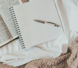 Pen resting on top of a notebook with blank pages on top of an open Bible