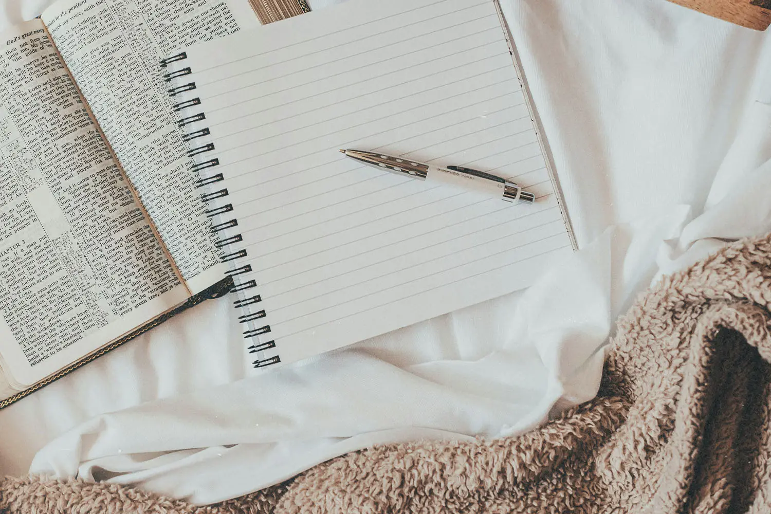 Pen resting on top of a notebook with blank pages on top of an open Bible