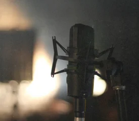 A close‑up of a studio microphone on a stand, lit from behind by a warm, blurred light source