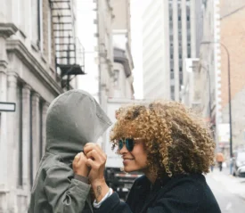 A person adjusts the hood of a child’s jacket on a city street lined with tall buildings, with a red French “Arrêt” stop sign visible in the background