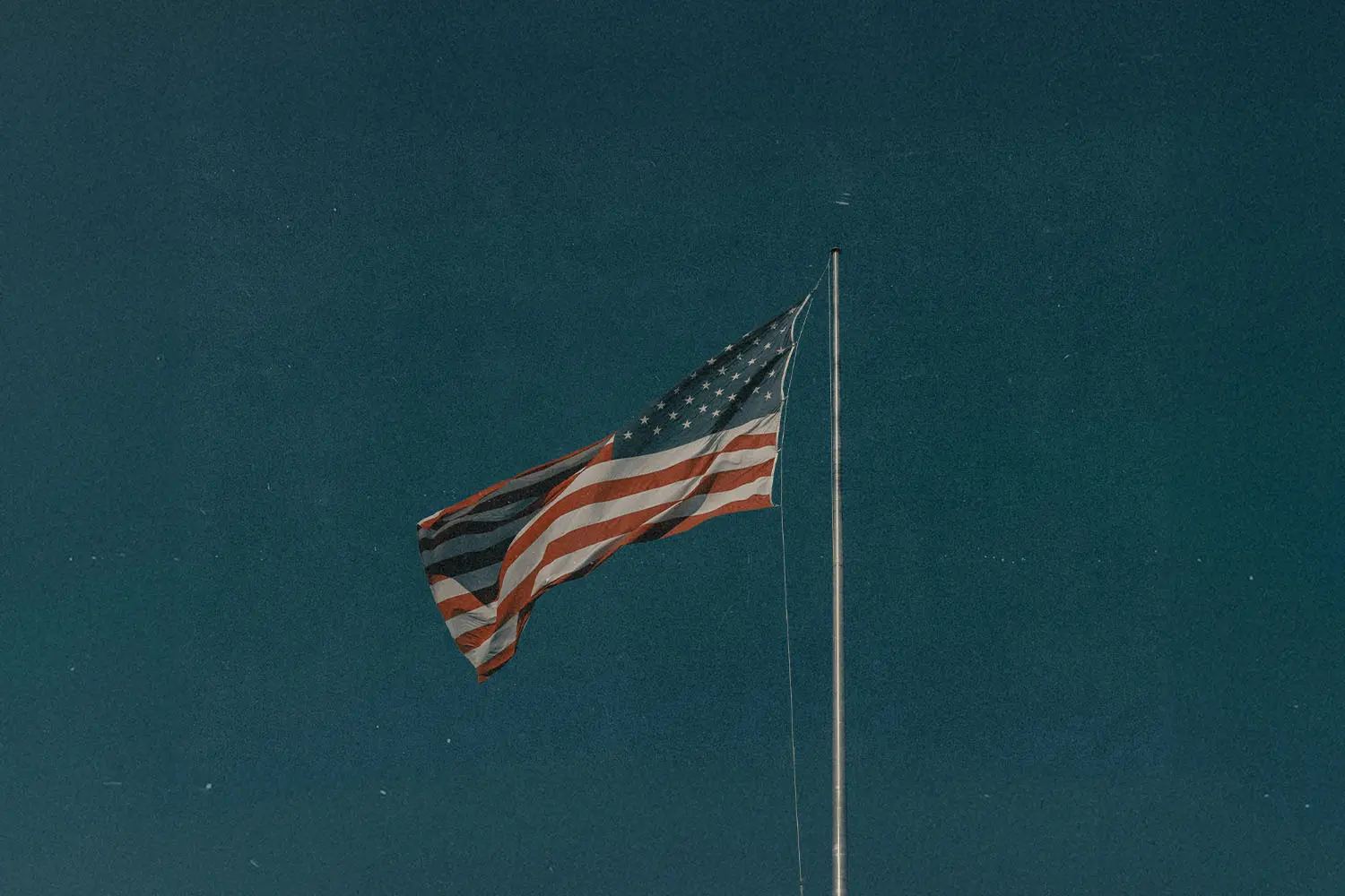 An American flag waving on a tall flagpole against a deep blue sky