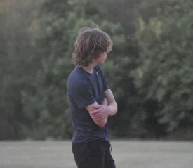 Teenage boy standing hunched with arms crossed looking away from the camera