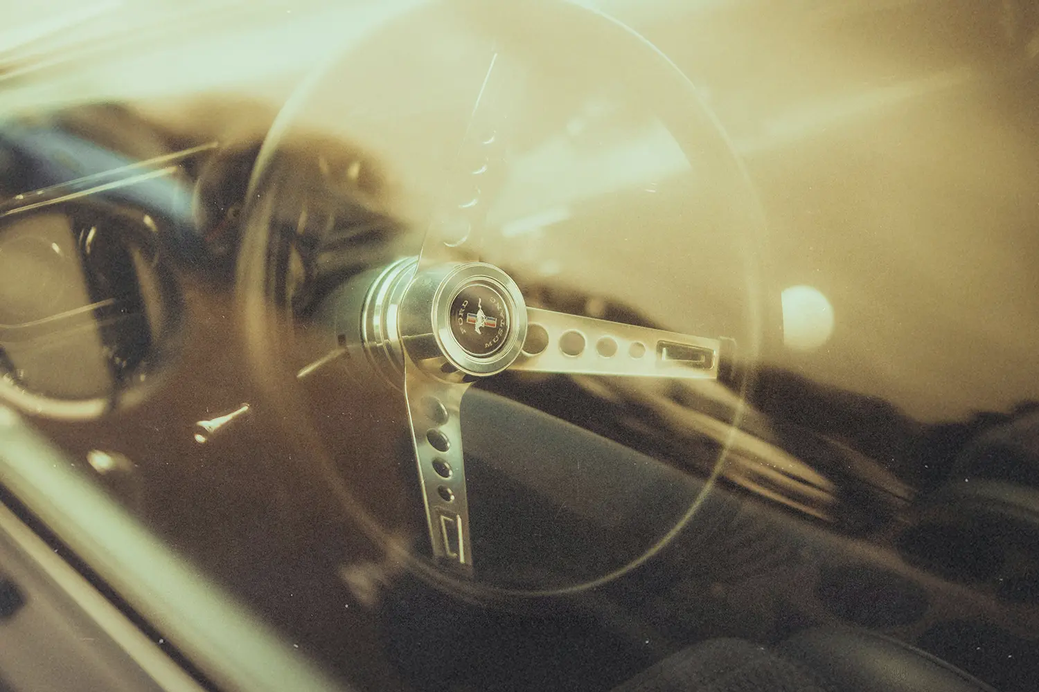 Vintage car steering wheel photographed through the windshield with warm golden reflections