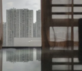 Window with curtains looking out to a body of water and apartment buildings in the distant background