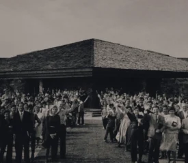Black-and-white photograph of a large group of KCM Staff gathered outdoors in front the Kenneth Copeland Ministries Chapel building, many with arms raised and waving toward the camera.