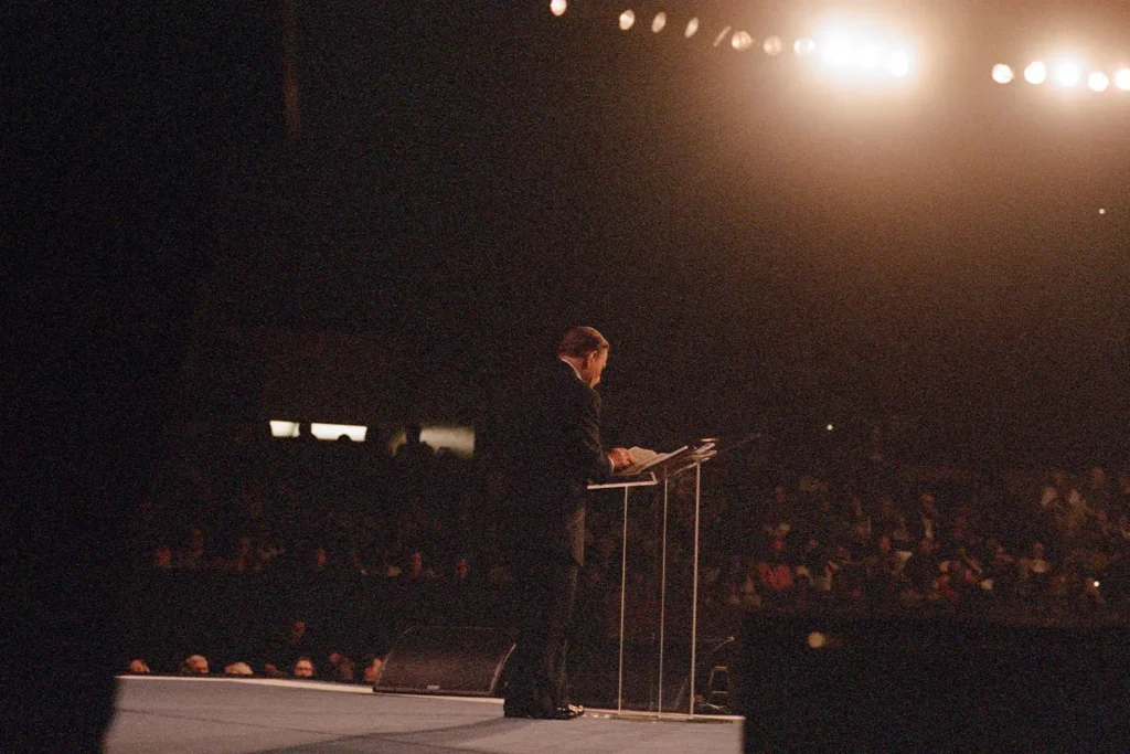 Kenneth Copeland standing at a platform preaching to a crowd