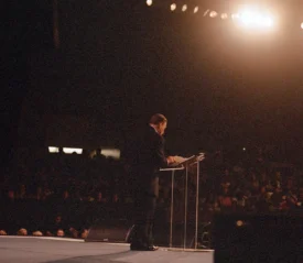 Kenneth Copeland standing at a platform preaching to a crowd